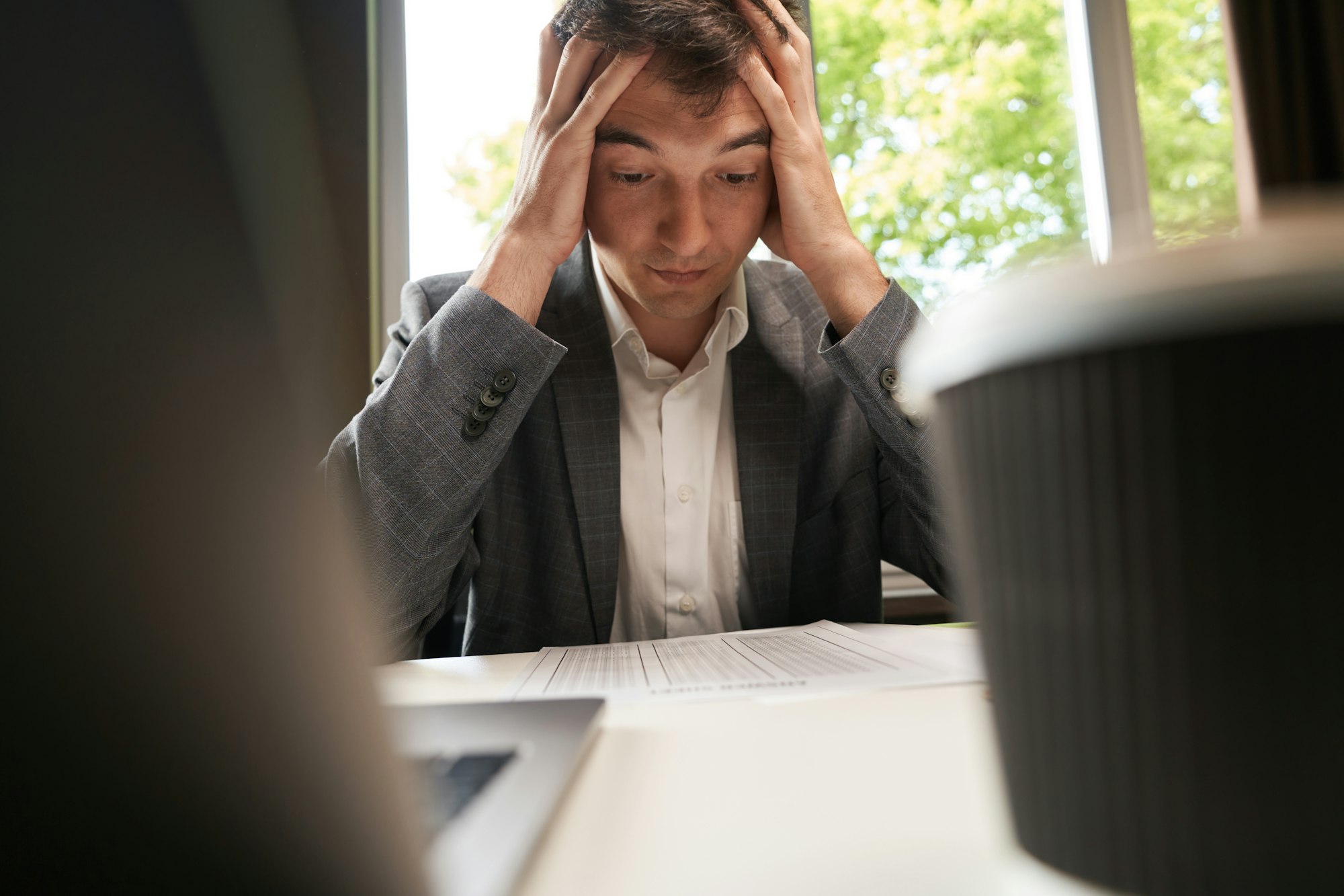 Male grabbing head in despair while looking at spreadsheet